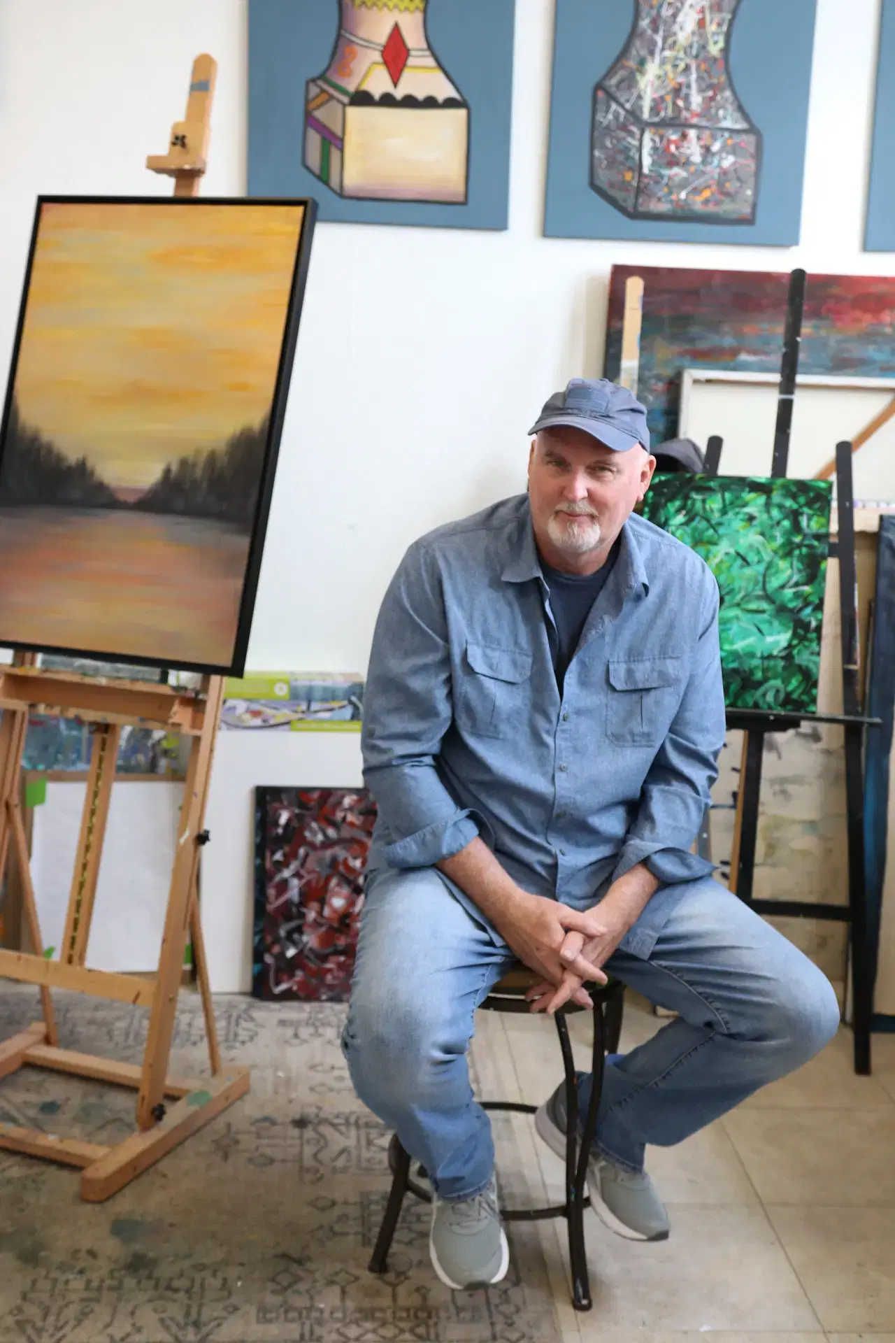Dennis Hood artist sitting on a chair with canvases in the background.